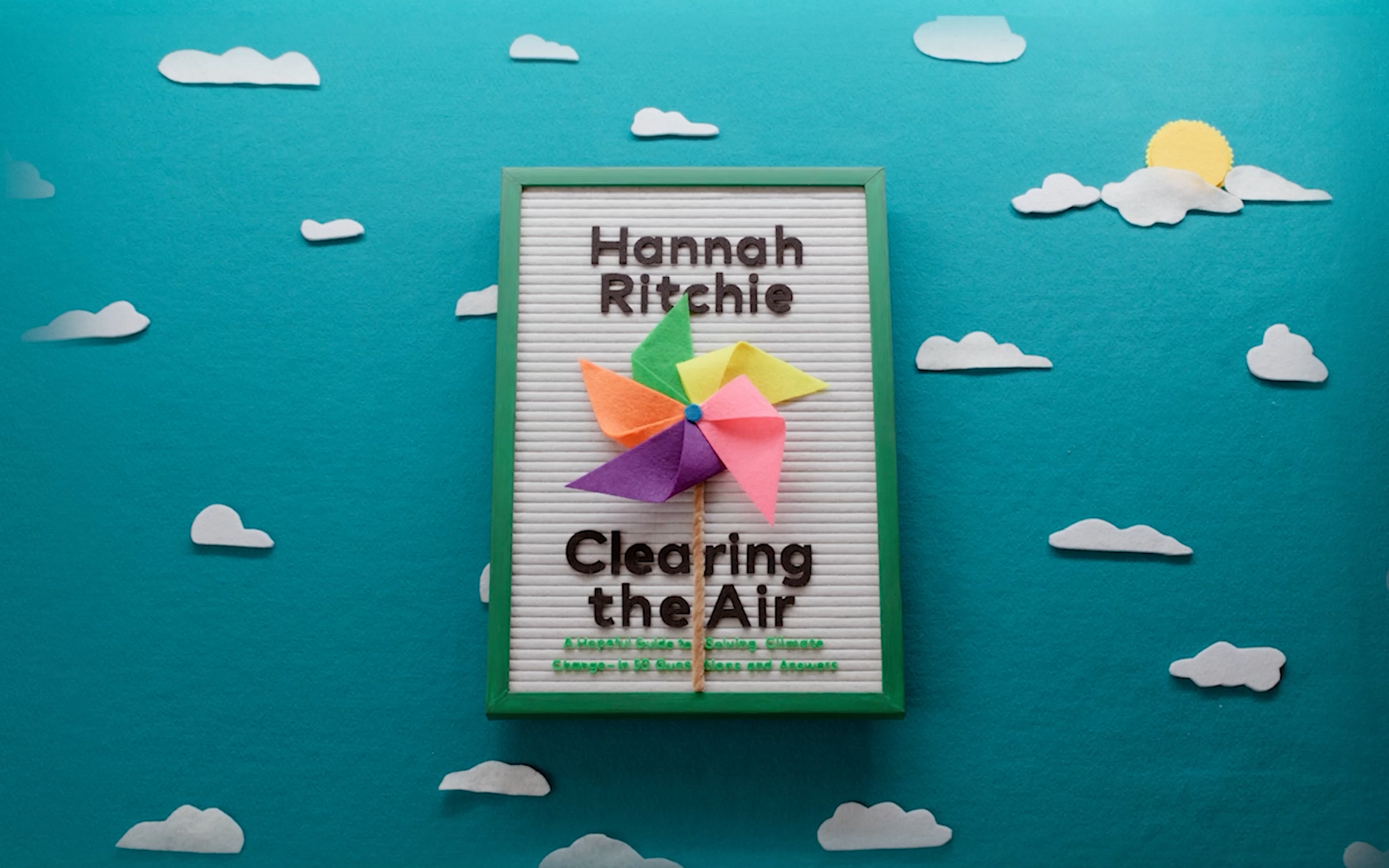 A felt sign depicting the cover of the book "Clearing the Air" by Hannah Ritchie with clouds in the background.