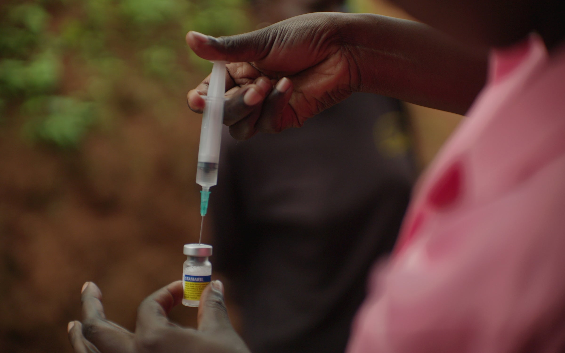 Agnes Nambozo holds a vaccine vial and draws it into a needle.