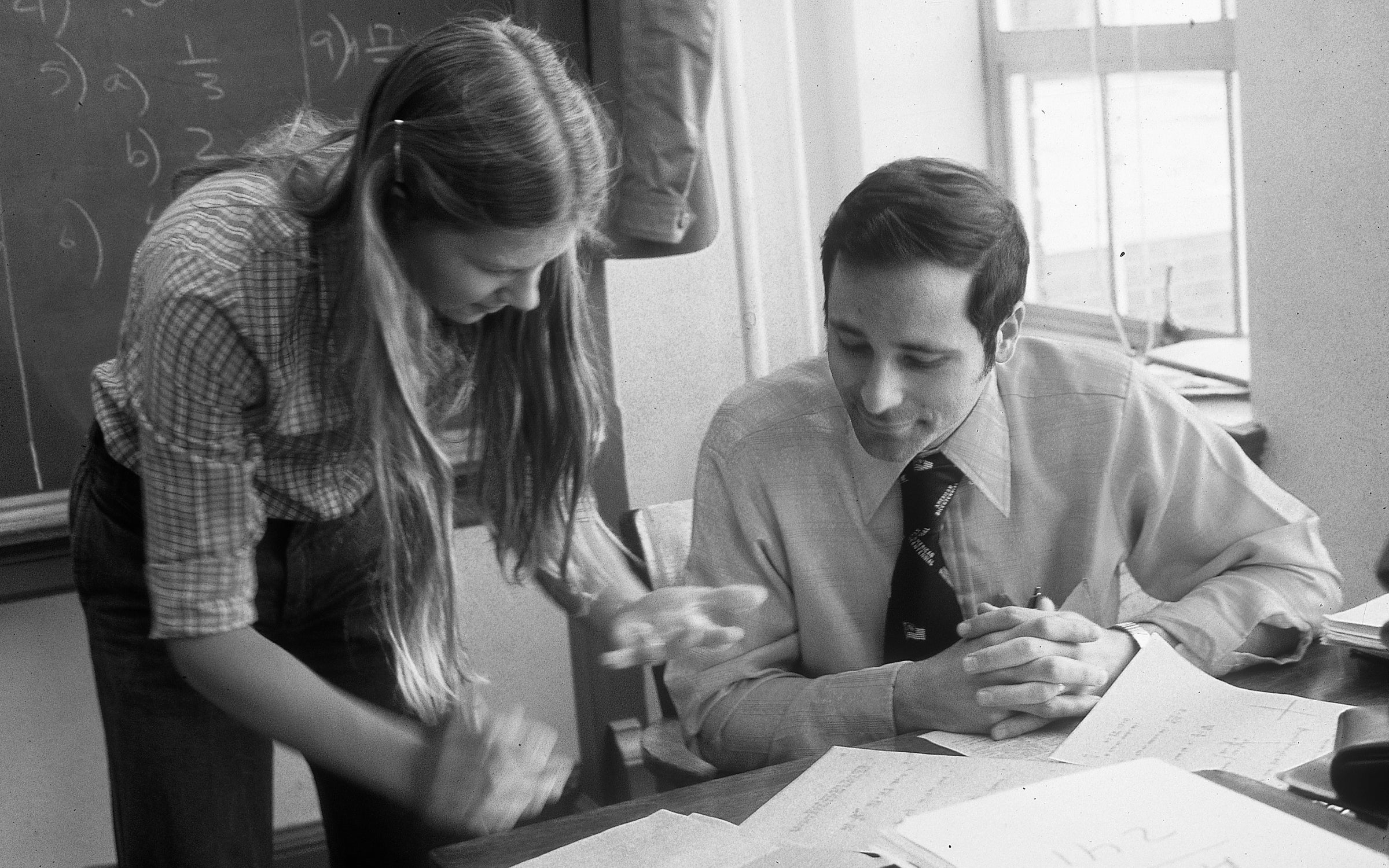 Paul Stocklin sitting at a desk working with a student standing next to him.