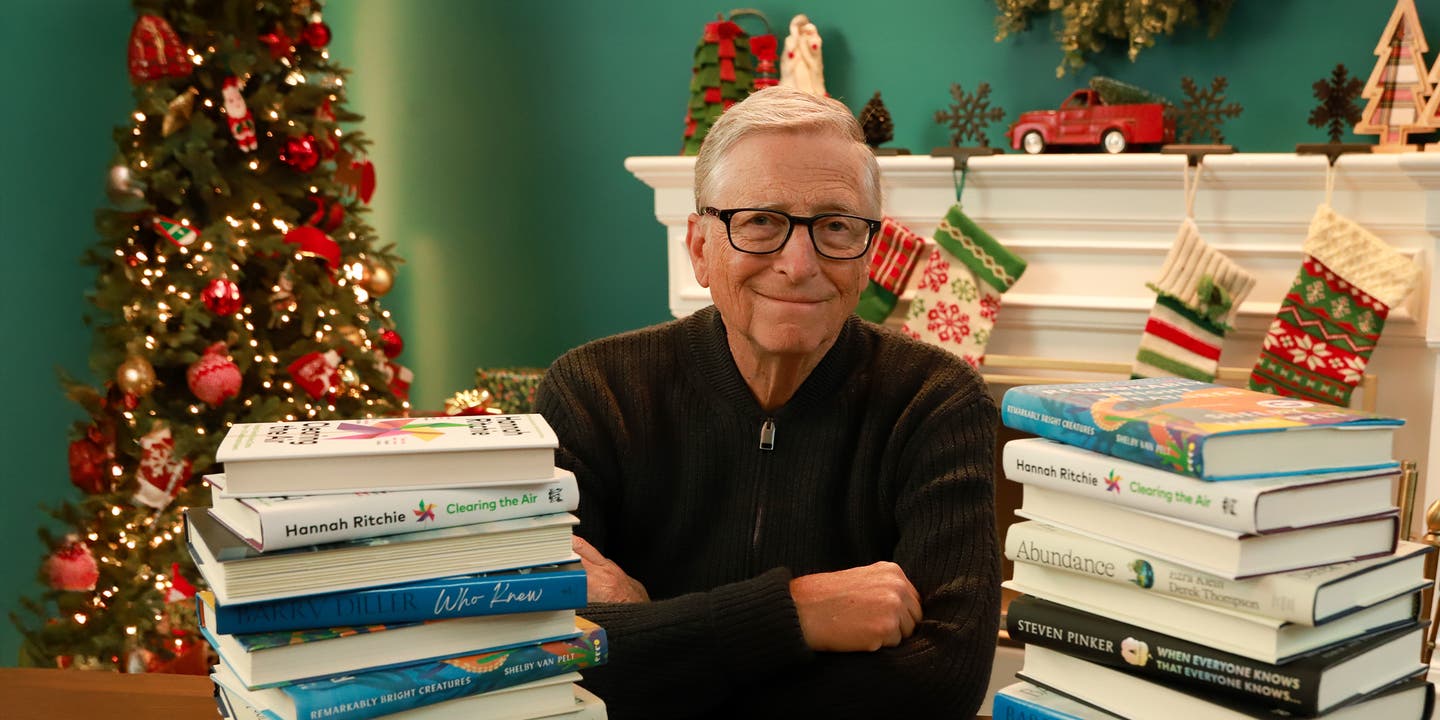 Bill Gates sitting at a table surrounded by holiday décor and stacks of books.