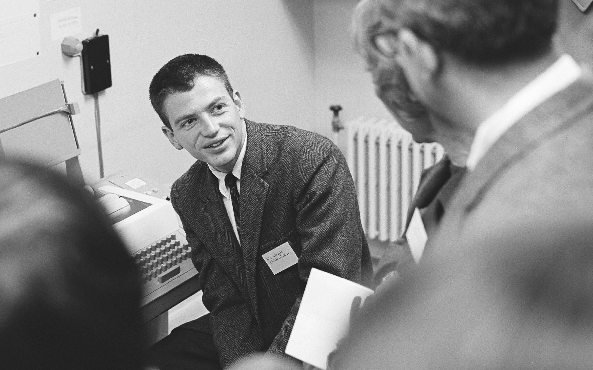 Fred Wright sitting in front of a Teletype ASR-33 computer looking at people behind him.