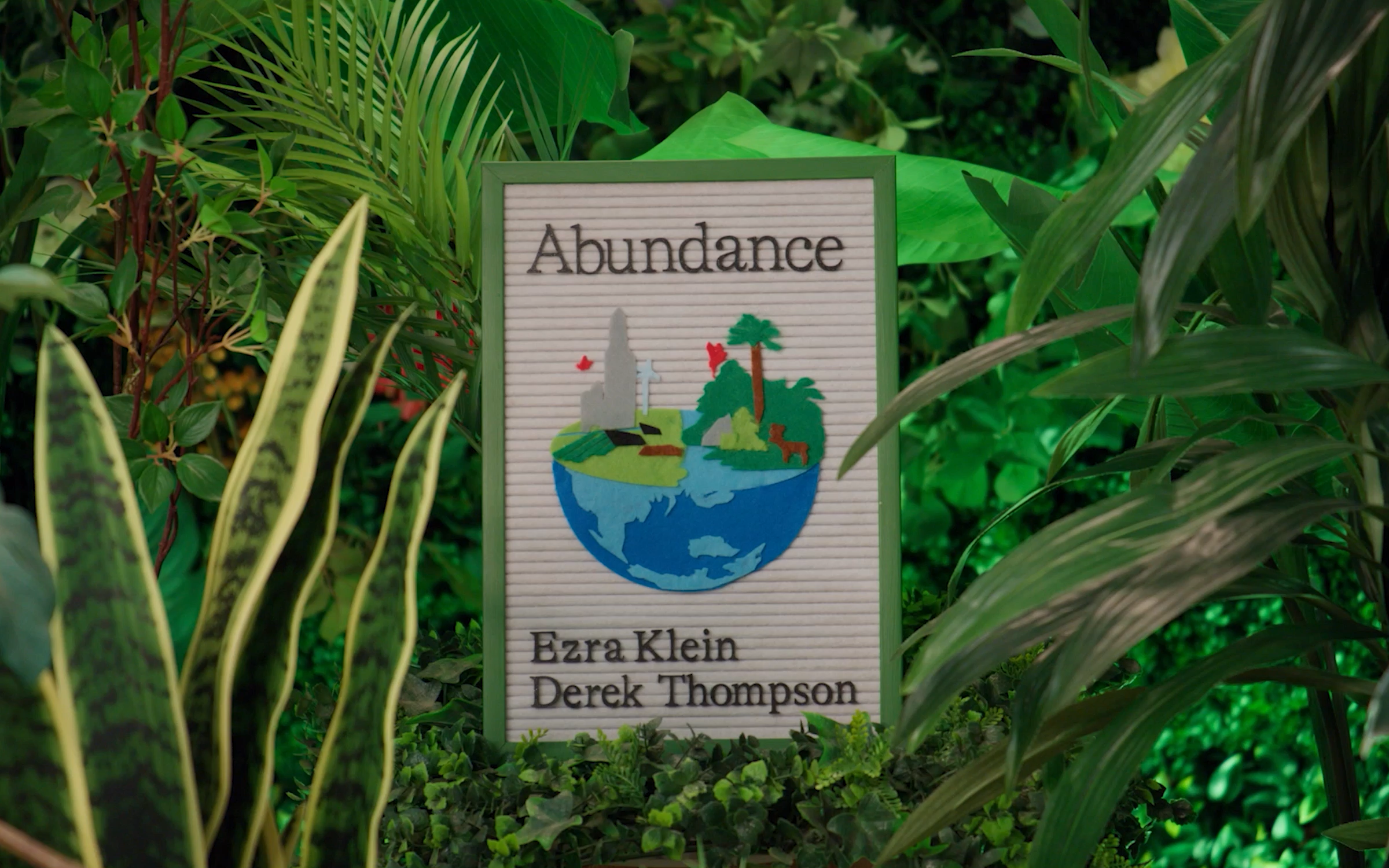 A felt sign depicting the cover of the book "Abundance" by Ezra Klein and Derek Thompson with plants in the background.