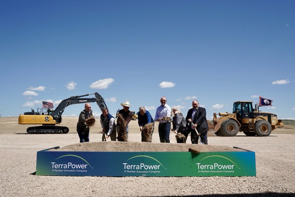 Bill Gates and other participants digging with shovels at the Natrium plant groundbreaking ceremony. A bulldozer and excavator are in the background, and the TerraPower sign is in foreground.