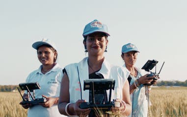 Three Drone Didis standing in a field holding drone controller devices.