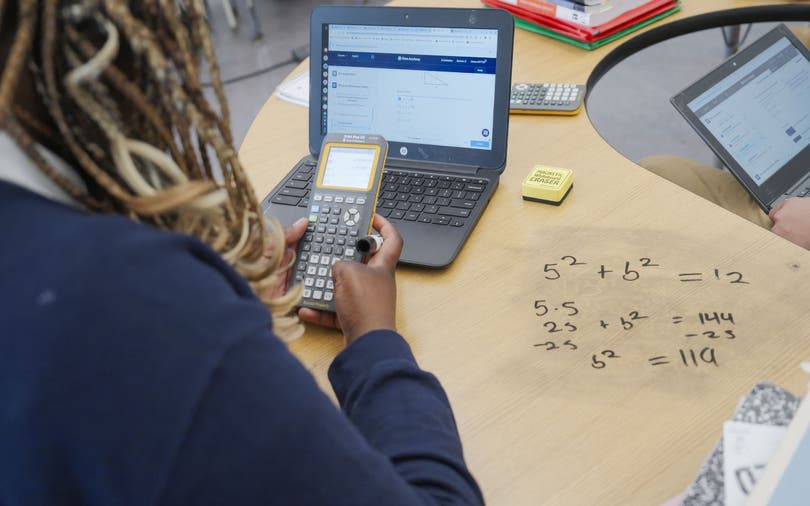 Over the shoulder view of a student using a calculator and a laptop with Khanmigo, an AI-powered education tool.