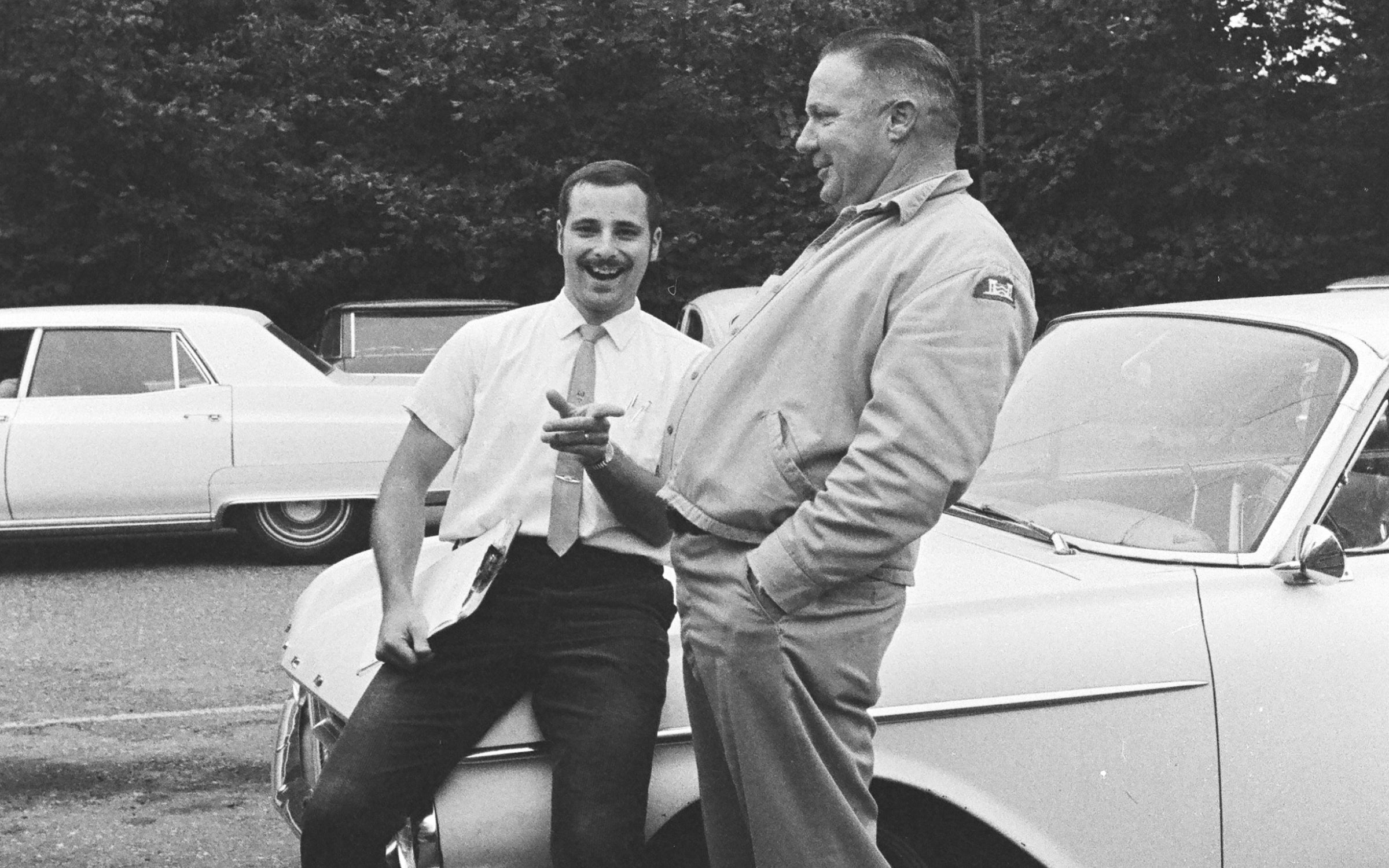 Paul Stocklin leaning on a car smiling and talking with another man.